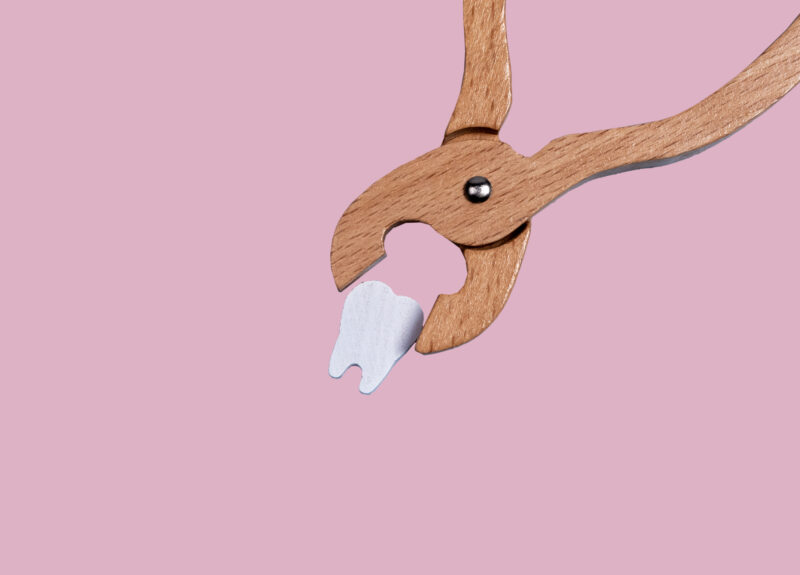 ピンク背景でペンチに挟まれる歯の模型