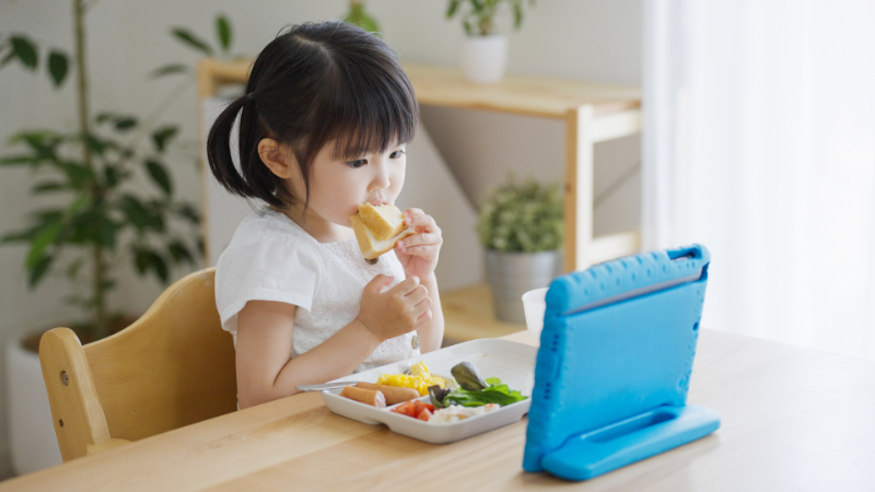 タブレットを見ながら食事をする子供