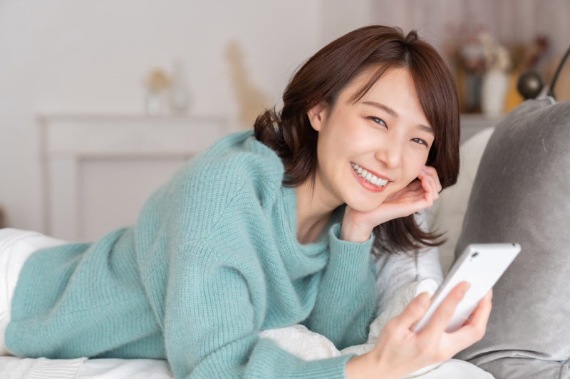部屋でスマホを見るリラックスした表情の女性