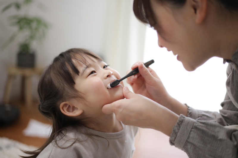 母親に仕上げ磨きをしてもらっている子ども