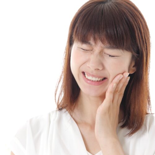 歯の根に膿が溜まって痛む頬を抑える女性