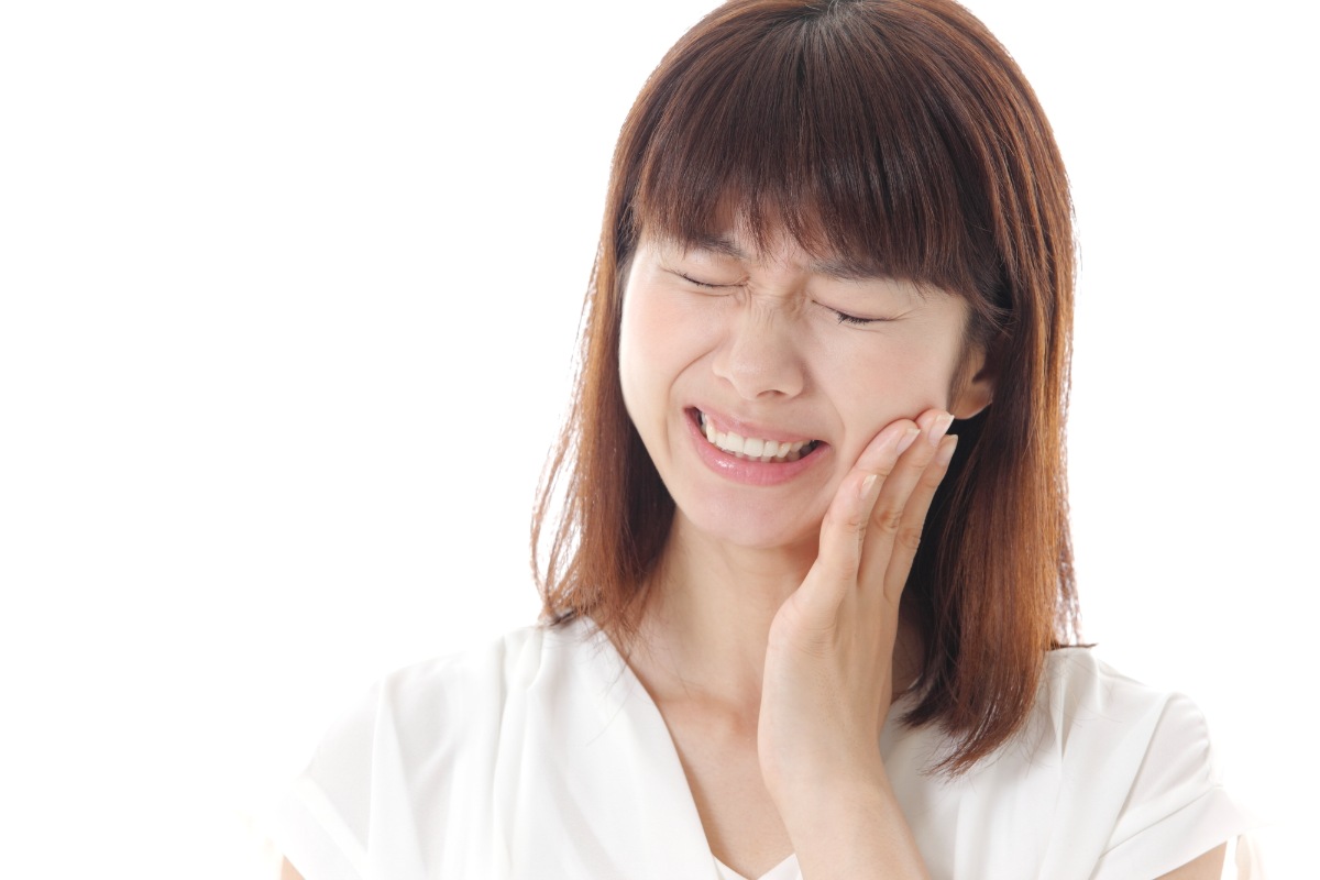 歯の根に膿が溜まって痛む頬を抑える女性